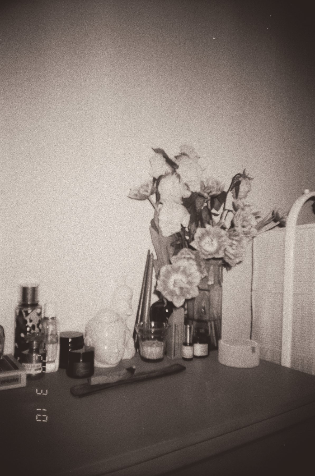 Penteadeira com perfumes, cremes, uma vela e um vaso de flores, em tons de sépia