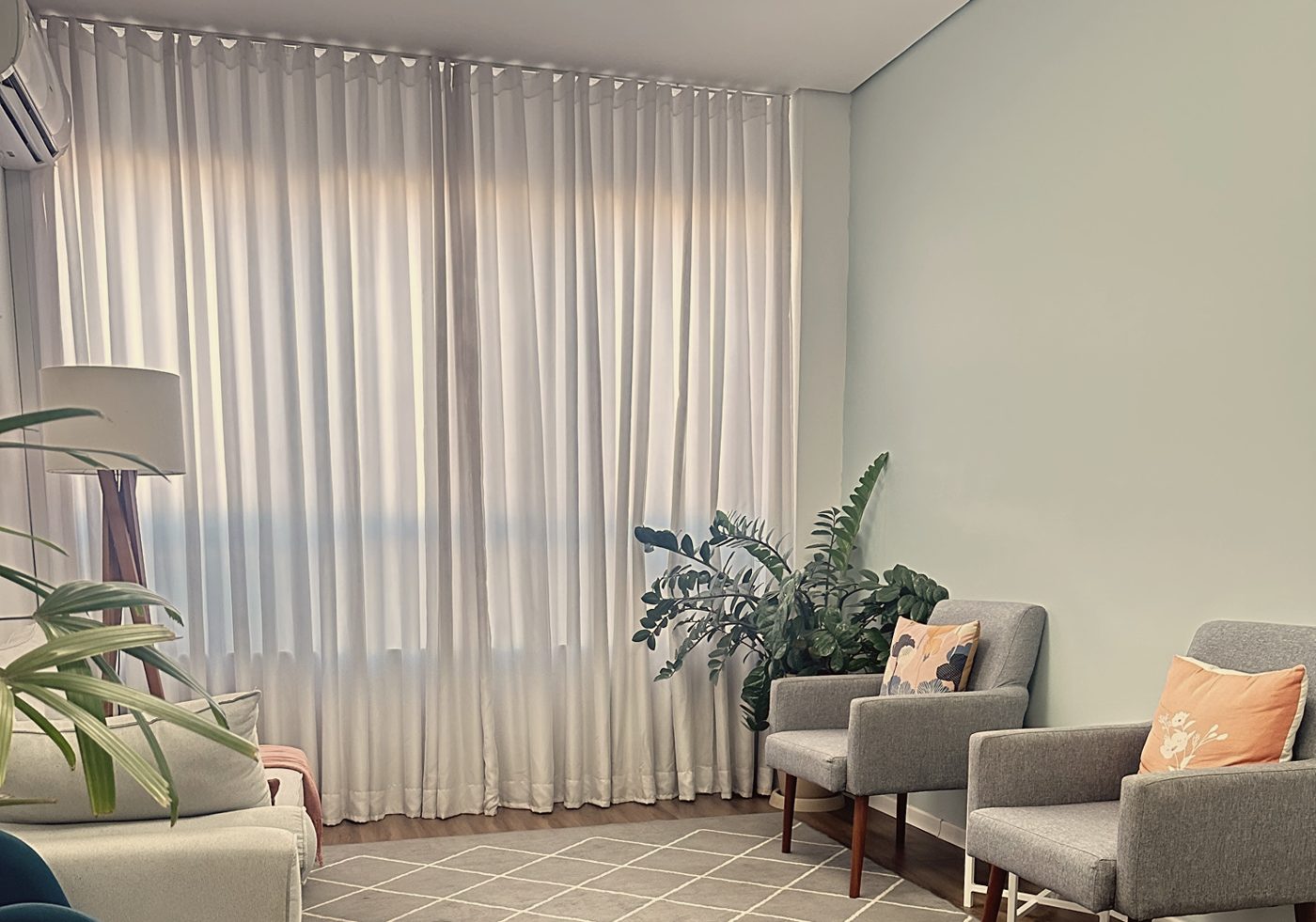 Sala do consultório, com poltronas, sofá, plantas e cortinas claras